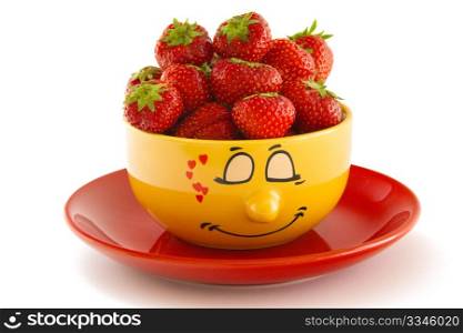 Yellow bowl with face print, on a red saucer filled with ripe red strawberries, isolated on white background