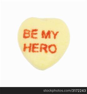 Yellow candy heart that reads be my hero against white background.