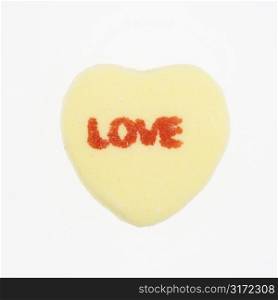 Yellow candy heart that reads love against white background.
