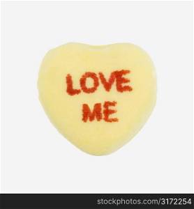 Yellow candy heart that reads love me against white background.