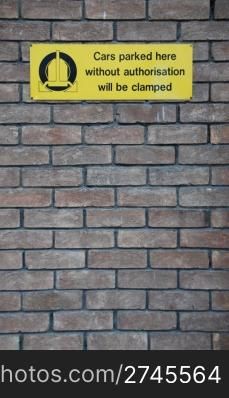 yellow cars parked here without authorisation will be clamped sign at a grey brick wall background