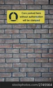 yellow cars parked here without authorisation will be clamped sign at a grey brick wall background
