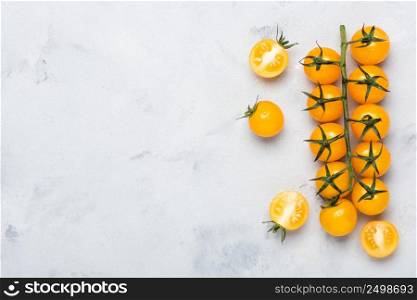 Yellow cherry tomatoes on branch, whole on cut in half, on rustic table top view with copy space.