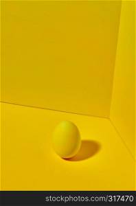 Yellow colored egg on a bright yellow background with shadow and space for text. Creative Easter Layout. A colored bright yellow egg on a yellow background with copy space and shadow reflection. Easter concept