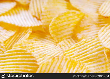 Yellow crispy ridged potato chips close up. Food background, banner, header, wallpaper.