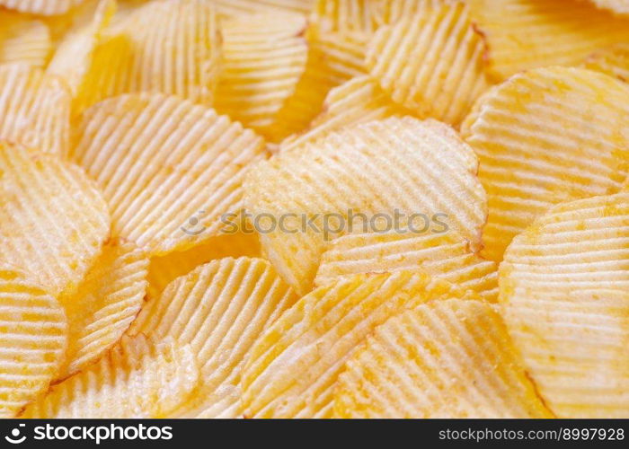 Yellow crispy ridged potato chips close up. Food background, banner, header, wallpaper.