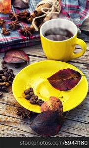 Yellow cup of black coffee on background with warm blanket strewn with autumn leaves. Black coffee in yellow cup