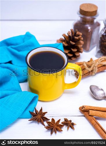yellow cup with black coffee and cinnamon on a white wooden table, top view
