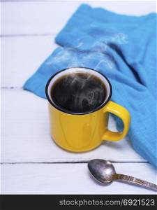yellow cup with black hot coffee on a white wooden table, top view