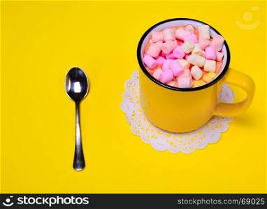Yellow cup with multi-colored marshmallow slices on a yellow background, top view