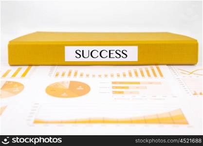 Yellow document binder with success word place on graphs, charts and business reports