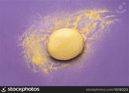 Yellow dough made of corn flour for cornbread on a purple background. Above view of cornbread dough and flour. Home cooking. European cornbread.