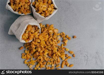 Yellow dry raisins spilled from textile sack on grey background. Spread dried fruit. Healthy eating concept. Wellness. Nutritious snack