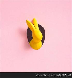 Yellow Easter bunny looks out of an egg-shaped hole in the pink background wall. Abstract concept. Square with copy space.. Yellow Easter bunny looks out of an egg-shaped hole in the pink background wall.