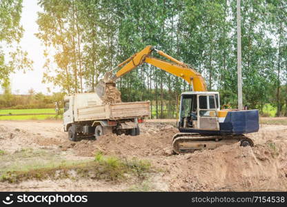 Yellow excavator machine loading soil into a dump truck at construction site