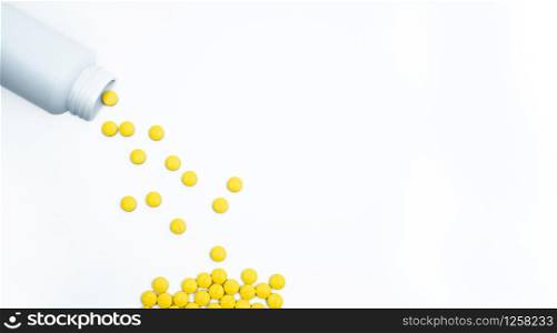 Yellow film coated tablets pills spilling out of pill bottle on white background with copy space. Painkiller tablet pills. NSAIDs pills for muscle pain.