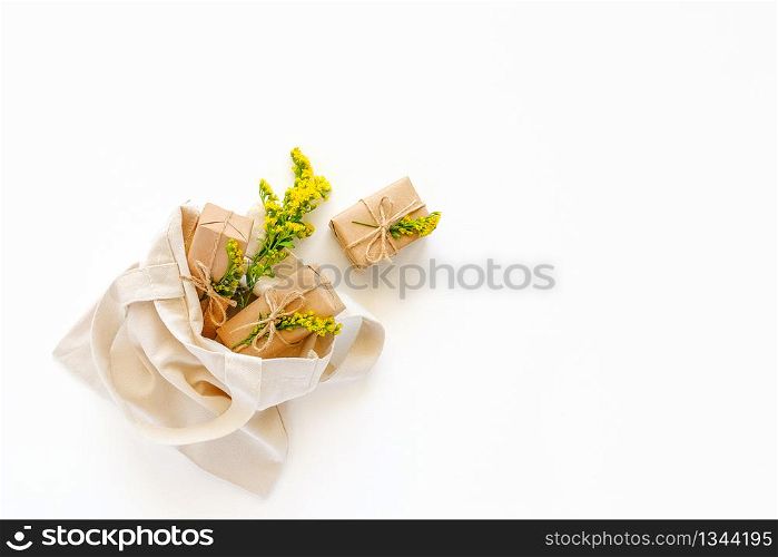 Yellow flowers and craft gifts fly out textile shopping bag on white background. Spring time, mothers day, womens day concept. Flat lay Top view Copy space.. Yellow flowers and craft gifts fly out textile shopping bag on white background. Spring time, mothers day, womens day concept. Flat lay Top view Copy space