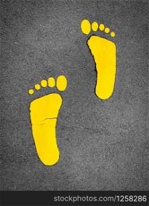 Yellow footprint painted on asphalt road. Walkway lane traffic sign. Foot mark on street texture background. Direction sign. Yellow footstep on tarmac floor. One step towards a better future concept.