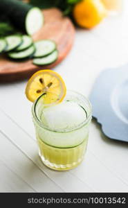 Yellow green drink in a rocks glass garnished with cucumbers and lemon