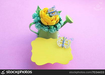 yellow handmade artificial flower, leaves with a glitter and a lot of paper roses in a miniature green watering can against a yellow background. and a purple butterfly view from the top. copy space.