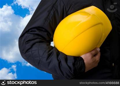 Yellow helmet at man hands on blue sky background