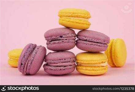 yellow in purple round baked macaroon cakes on a pink background, dessert stands in a stack, delicious