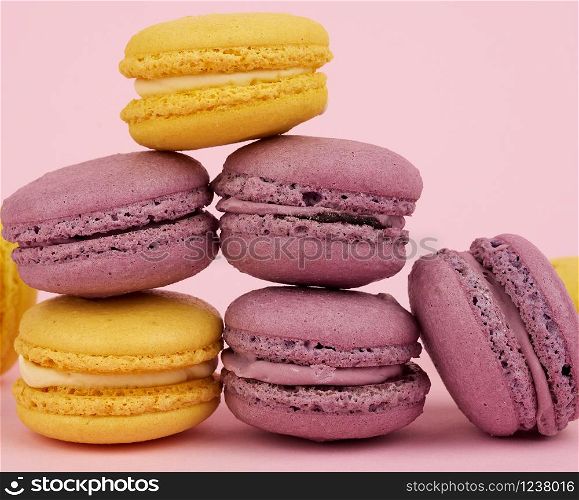 yellow in purple round baked macaroon cakes on a pink background, dessert stands in a stack, close up