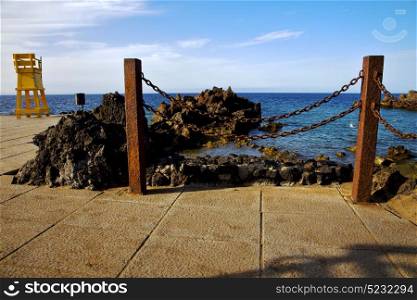 yellow lifeguard chair cabin in spain lanzarote rock stone sky cloud beach water musk pond coastline and summer