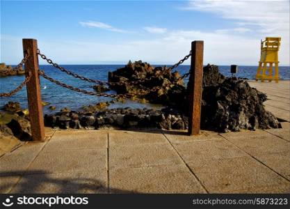 yellow lifeguard chair cabin in spain lanzarote rock stone sky cloud beach water musk pond coastline and summer &#xA;