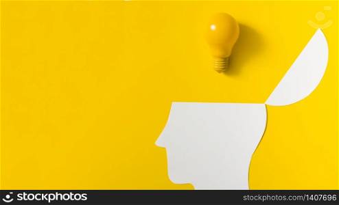 Yellow light bulb over the open paper cut out head against colored background
