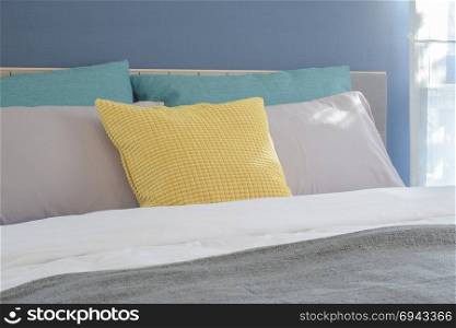 Yellow, light gray and green pillows setting on bed in modern interior bedroom