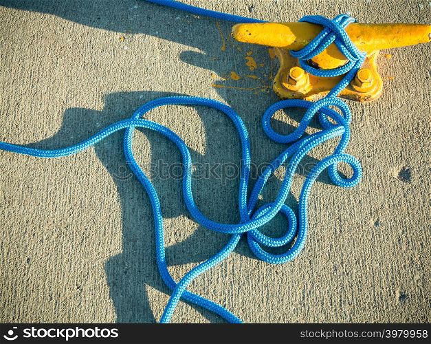 Yellow mooring bollard with blue rope in marina closeup