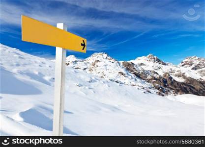 Yellow mountain guidepost along an alpine pathway over a snowy landscape in a clear winter day. Italian Alps, Val d&rsquo;Aosta, Italy.
