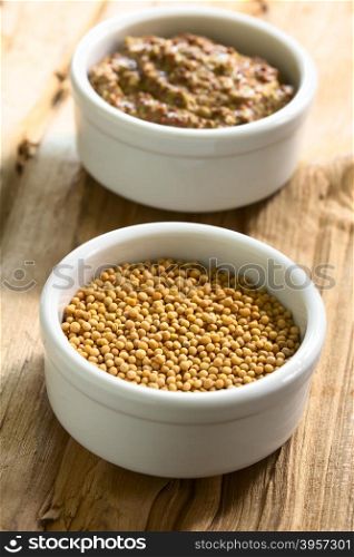 Yellow mustard seeds and whole grain mustard in small bowls, photographed on wood with natural light (Selective Focus, Focus one third into the seeds)