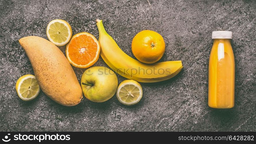 Yellow organic fruits smoothie with lemon, oranges, apple, mango and banana in bottle on gray granite table , top view. Healthy dieting and antioxidant beverage