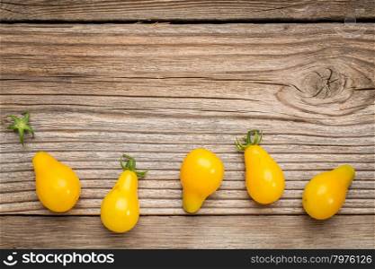 yellow pear tomato - a row of fruits on a grained weathered wood with a copy space