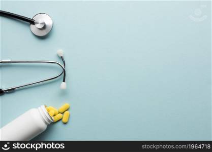 yellow pills spilling out from white bottle near stethoscope blue surface. High resolution photo. yellow pills spilling out from white bottle near stethoscope blue surface. High quality photo