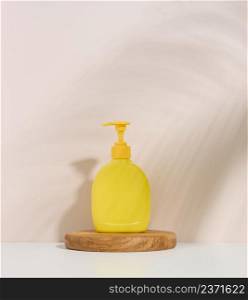 Yellow plastic container with a dispenser on a beige background. Yellow container for liquid soap, shampoo