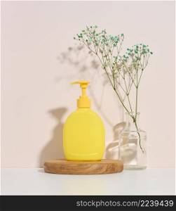 yellow plastic container with a dispenser on a wooden background and palm branch on a beige background. Container for liquid soap, shampoo