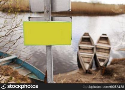 yellow plate for inscription on grass by the river and boats background on early spring day.. yellow plate for inscription on grass by the river and boats background on early spring day