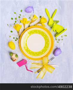 Yellow plate with easter egg decoration, sign and flowers on gray wooden background, top view, place for text