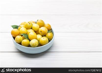 Yellow plum mirabelle fruit in bowl on white wooden table. Copy space. Healthy food