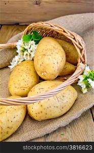 Yellow potato tubers with a flower in a wicker basket on a sacking on a wooden board