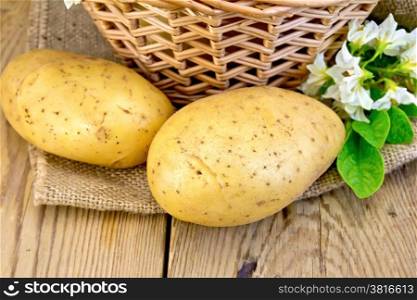 Yellow potato tubers with a flower on burlap, wicker basket on a wooden board