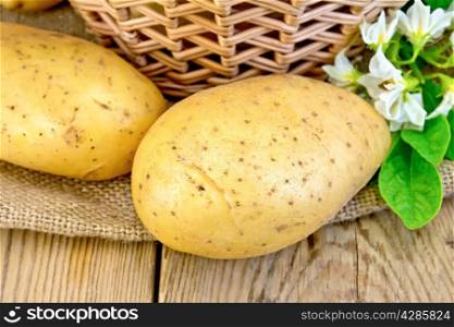 Yellow potato tubers with a flower on burlap, wicker basket on the background of wooden boards
