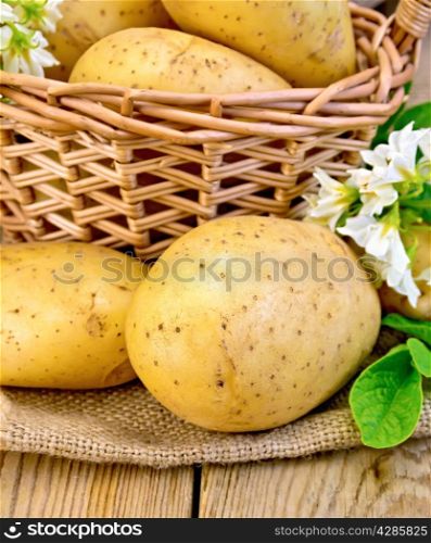 Yellow potato tubers with a flower on sackcloth, and in a wicker basket on a wooden board