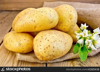 Yellow potato tubers with a flower on sacking on a wooden boards background