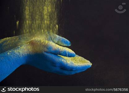 Yellow powder falling on blue cupped hands against black background