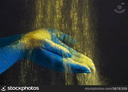 Yellow powder falling on blue cupped hands over black background