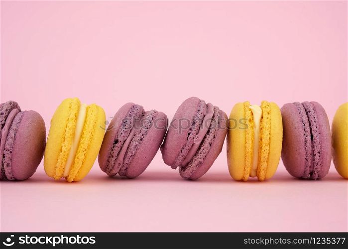 yellow, purple round baked macarons cakes on a pink background, dessert lies in a row, close up